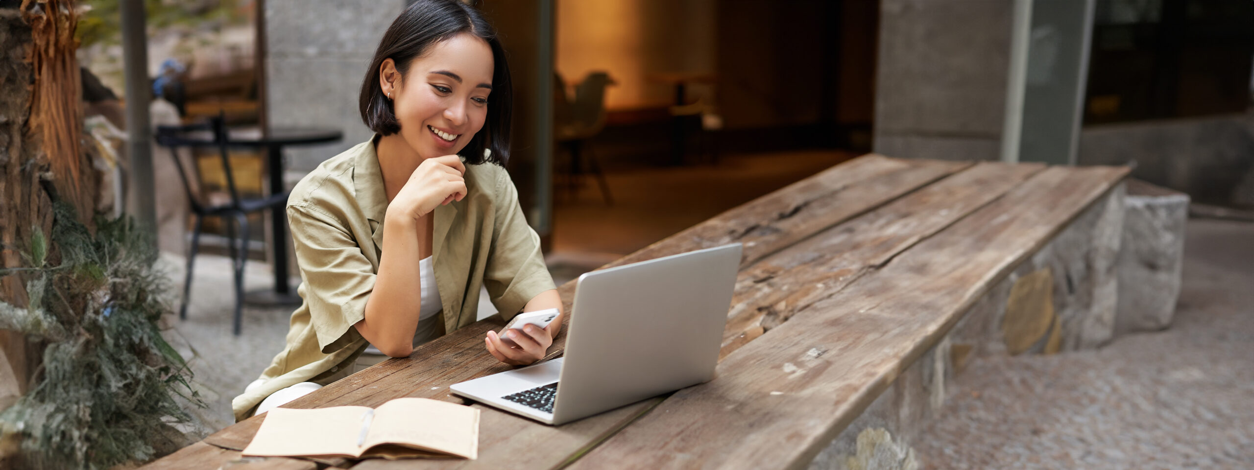Portrait of stylish urban woman working on laptop from outdoor cafe, sitting with documents and computer, smiling